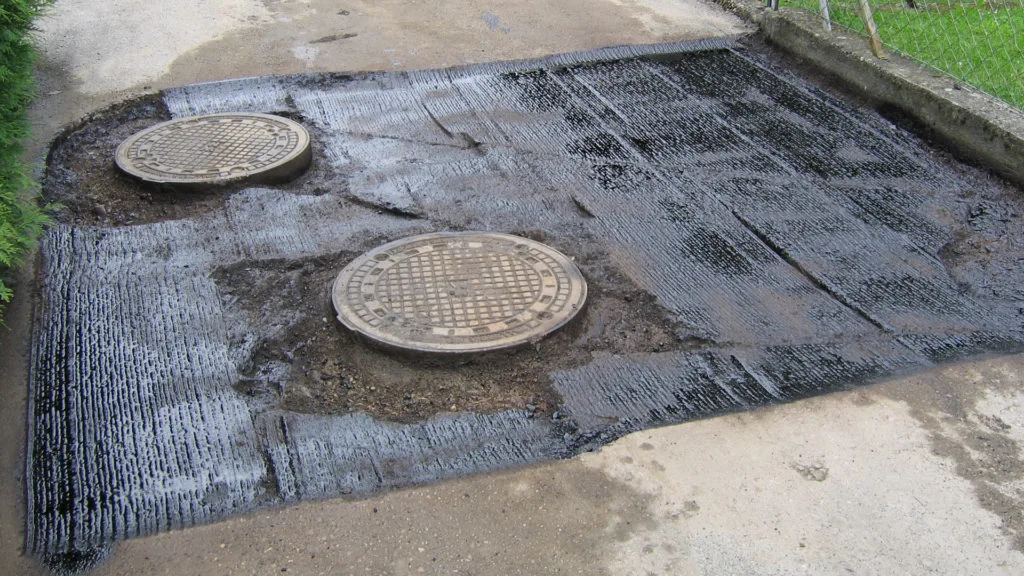 Reparierte Straßenoberfläche mit zwei Schachtdeckeln, die in frischem Asphalt eingebettet sind, zeigt die Straßeninstandhaltung.