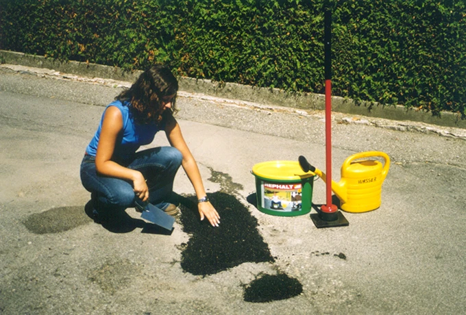 Rephalt Asphalt Reparaturset mit einer Frau, die Asphalt auf einer Straße verarbeitet, inklusive Werkzeug und Materialien.